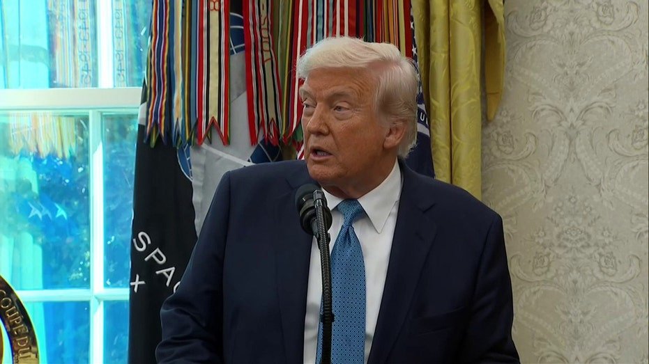 donald trump wearing blue suit and tie talks in front of microphone in oval office