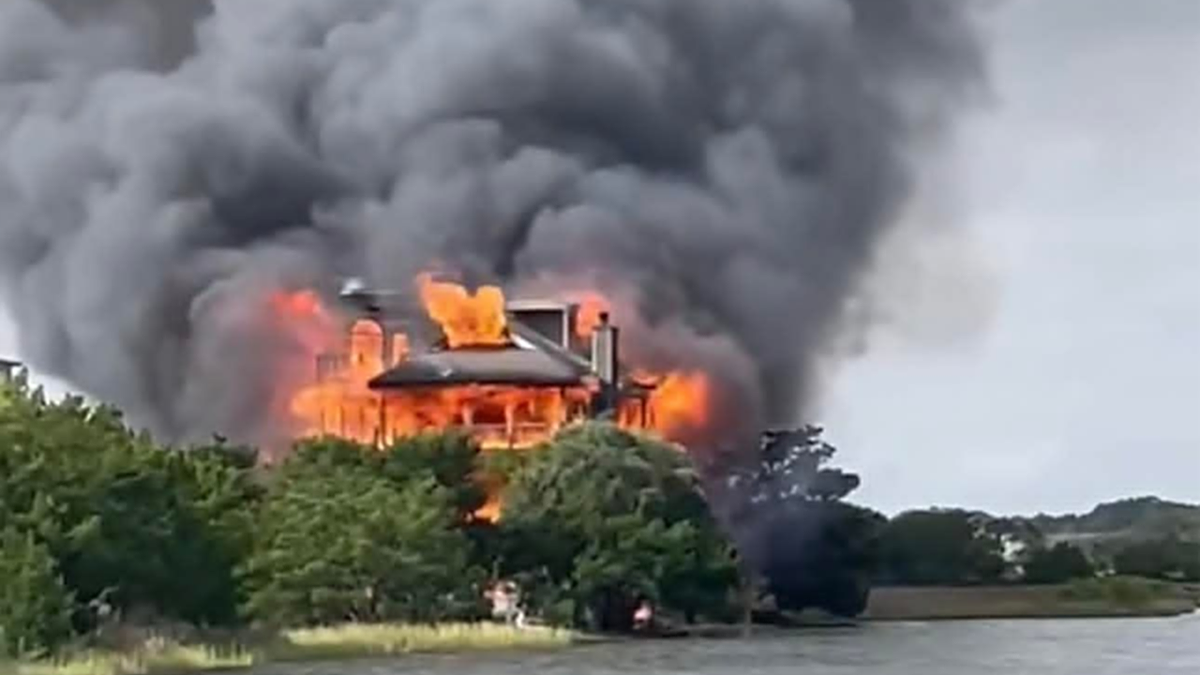 Flames and dark smoke billowing out of a waterfront mansion