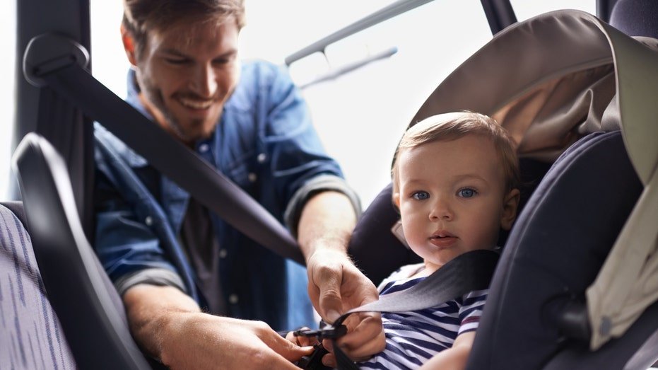 A young father strapping his baby into a car