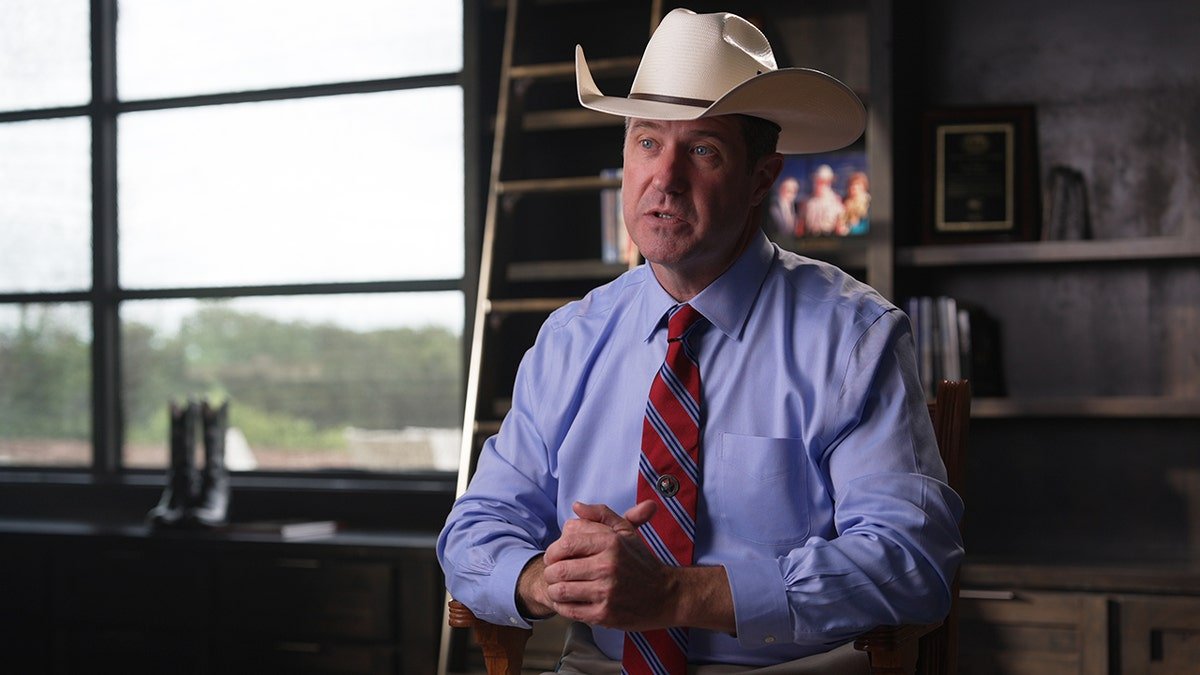 Texas Ranger Jim Holland with his cowboy hat on, with cowboy boots in the background.