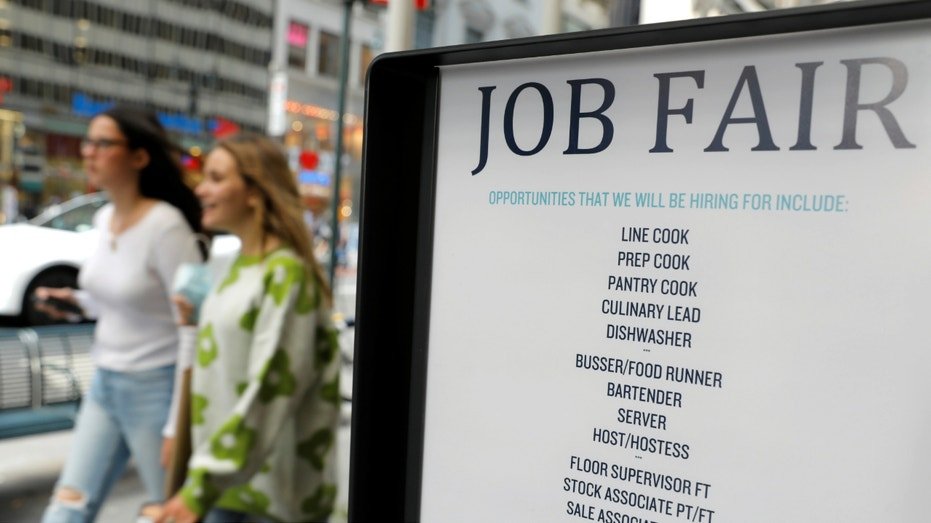 A job fair sign as people walk by in the background.