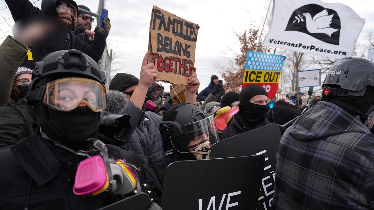 Protesters in riot gear holding signs