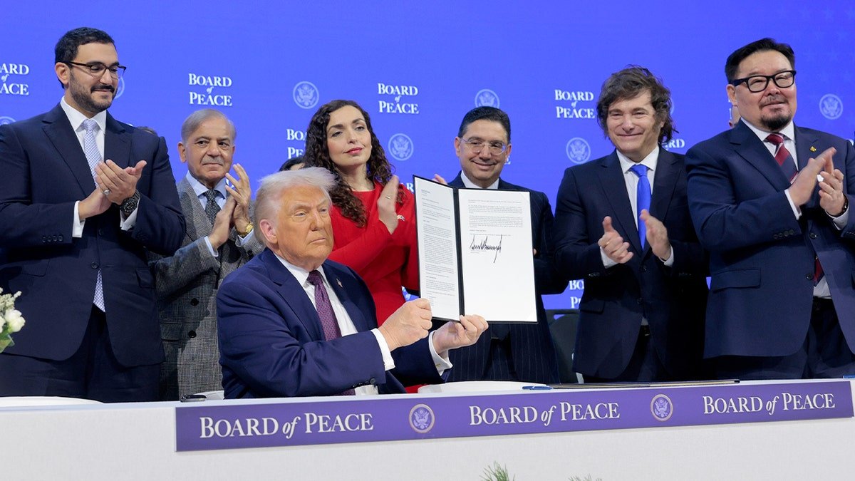 The U.S. president raises a signed document during a formal diplomatic event at an international forum.
