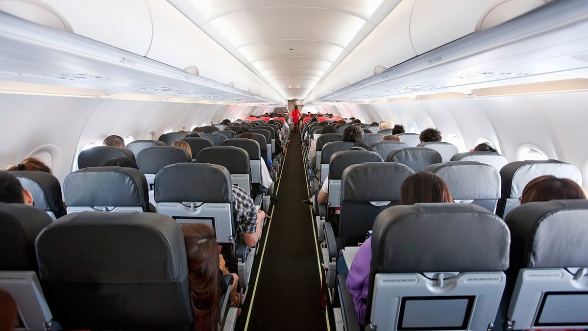 Interior of a commercial airplane cabin with passengers seated in rows during a flight.