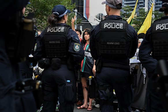 A protester raises her arm in the air, making the peace sign whilst facing a line of NSW police officers during the protests at Sydney’s Town Hall against the visit of Israeli President Isaac Herzog.