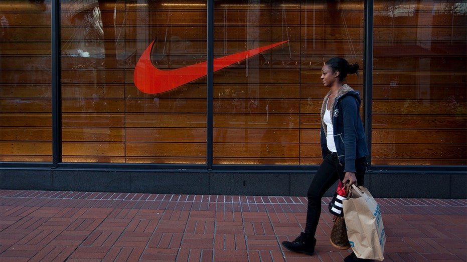 A woman walking with a shopping bag in front of a Nike store.