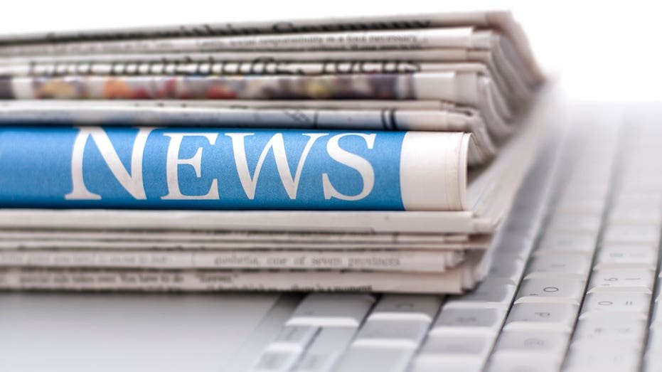 A stack of newspaper sits on top of a computer keyboard