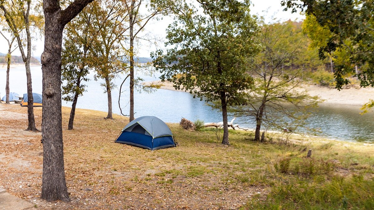 Tent campsite beside a calm lake surrounded by trees in early autumn.