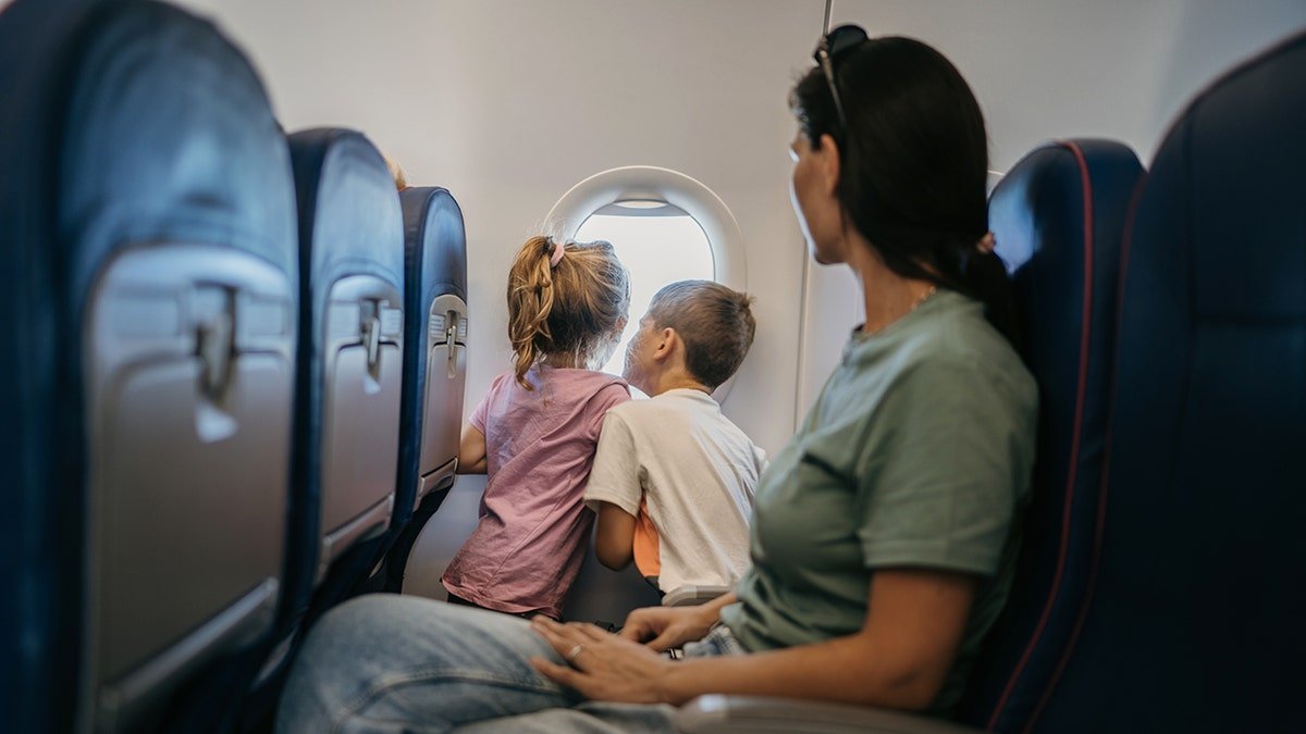 Mother and two children looking out airplane window while seated on a commercial flight.