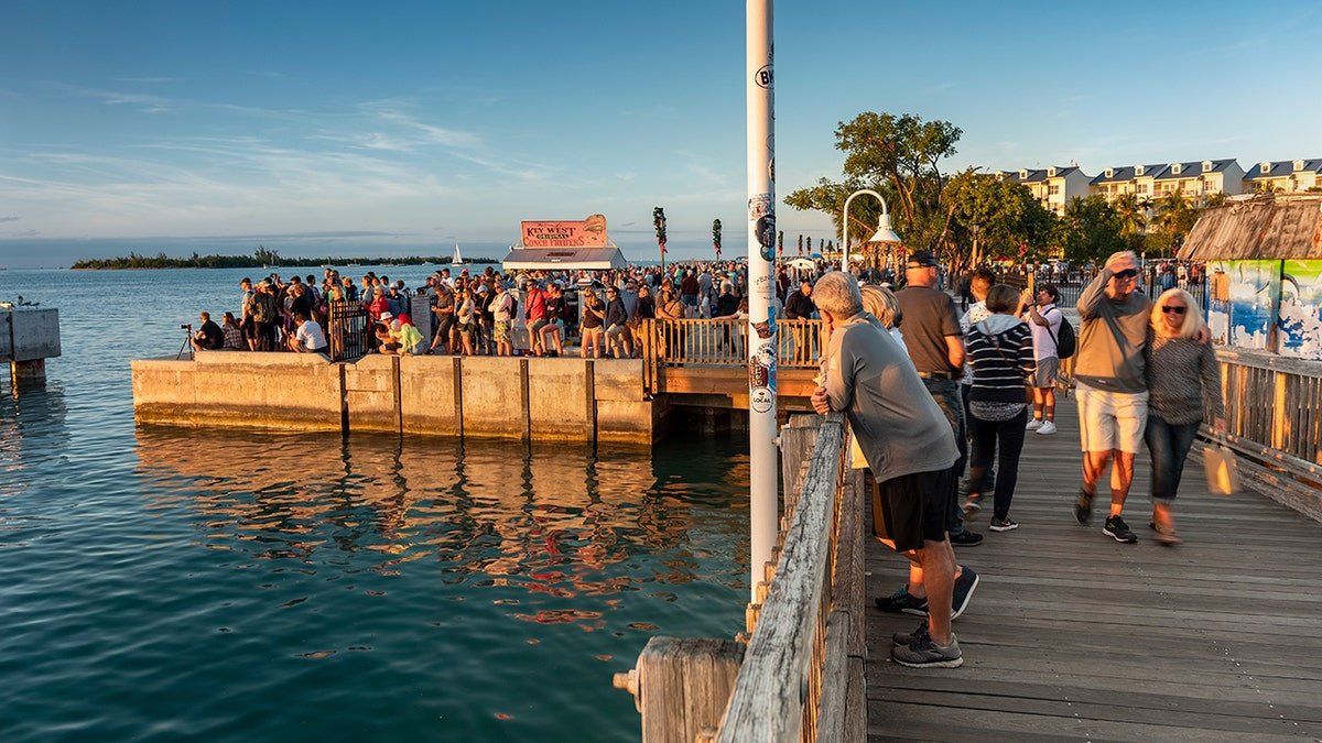 Crowded waterfront pier at sunset in Key West, Florida, with tourists gathered by the ocean.
