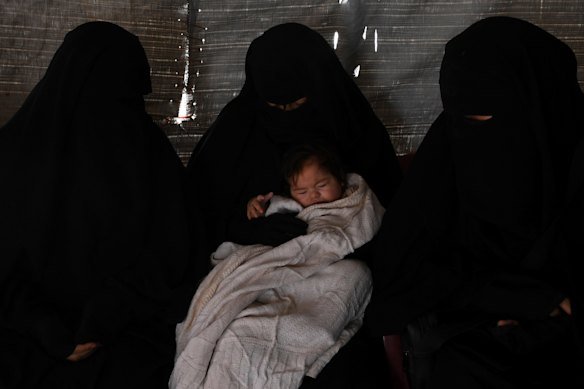 Kawsar Abbas (left), and Zeinab Ahmed (right) look down at baby Layla in al-Hawl camp in 2019.