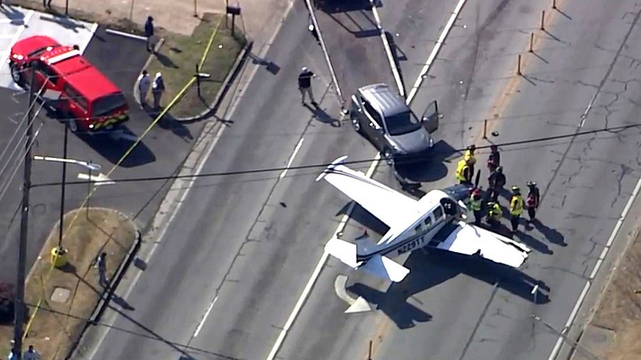 Aerial view of small plane surrounded by emergency crews after roadway landing.