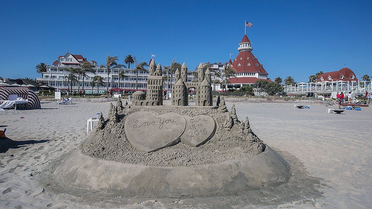 A detailed sandcastle with heart-shaped carvings reading 