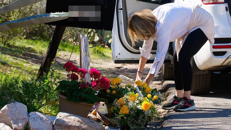 A woman placing yellow flowers on the ground outside Nancy Guthrie’s home.