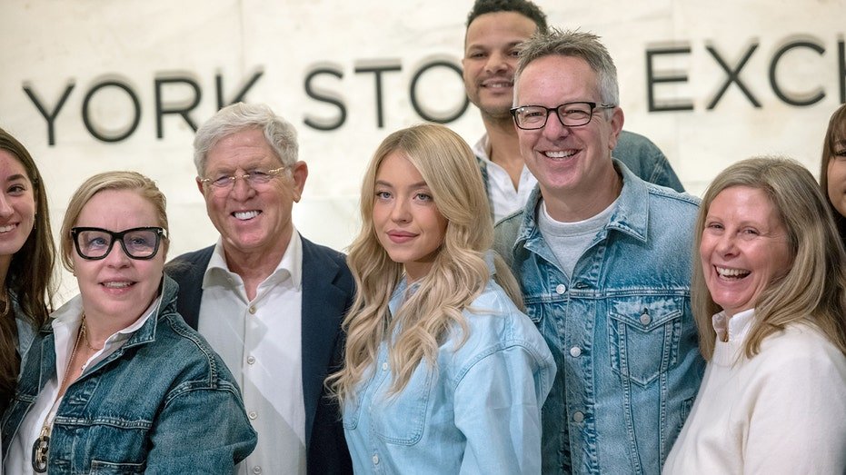 Sydney Sweeney poses beside executives inside the NYSE trading floor during a ceremonial bell ringing.