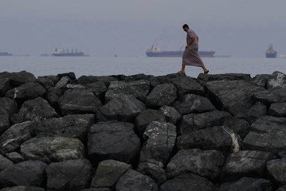 A man walks along the shore as oil tankers and cargo ships line up in the Strait of Hormuz.
