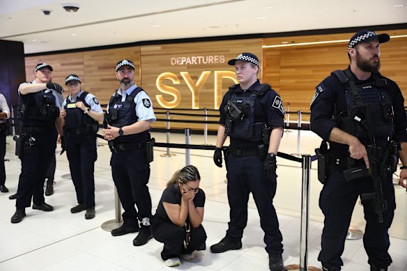 A supporter of the Iranian women’s soccer team is crouched in distress at the knees of police officers at Sydney International Airport.