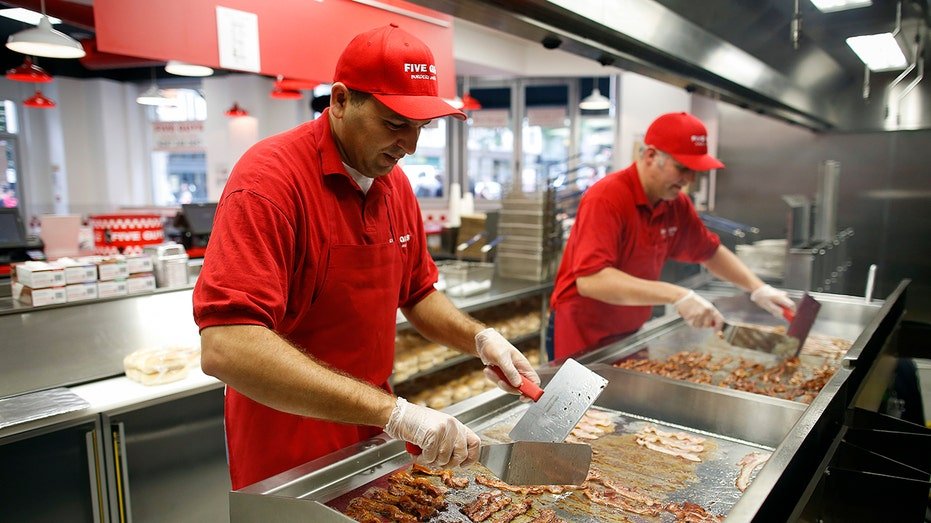 Chefs fry bacon on a griddle in the kitchen at U.S. burger restaurant chain Five Guys