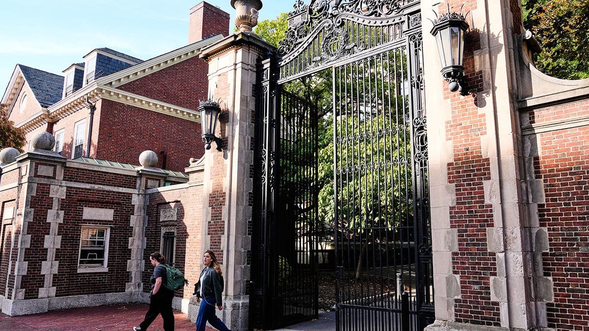 Harvard students walking through gate surrounded by brick wall and building