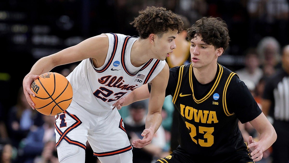 Illinois basketball player dribbles while an Iowa Hawkeyes players defends