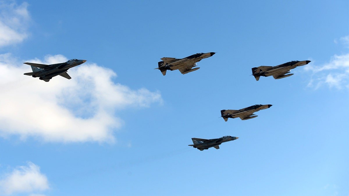 Two military jets and additional aircraft bank in tight formation during a demonstration flight over Kish Island.