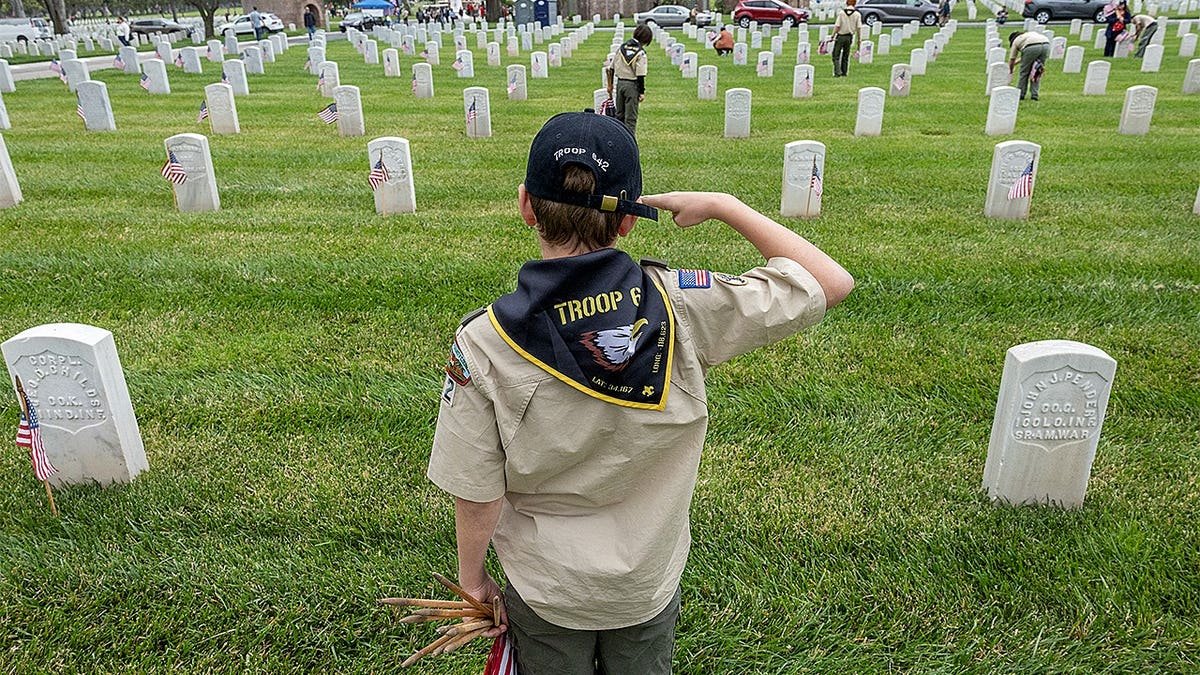 Julian Holkenborg saluting after planting a flag at Los Angeles National Cemetery