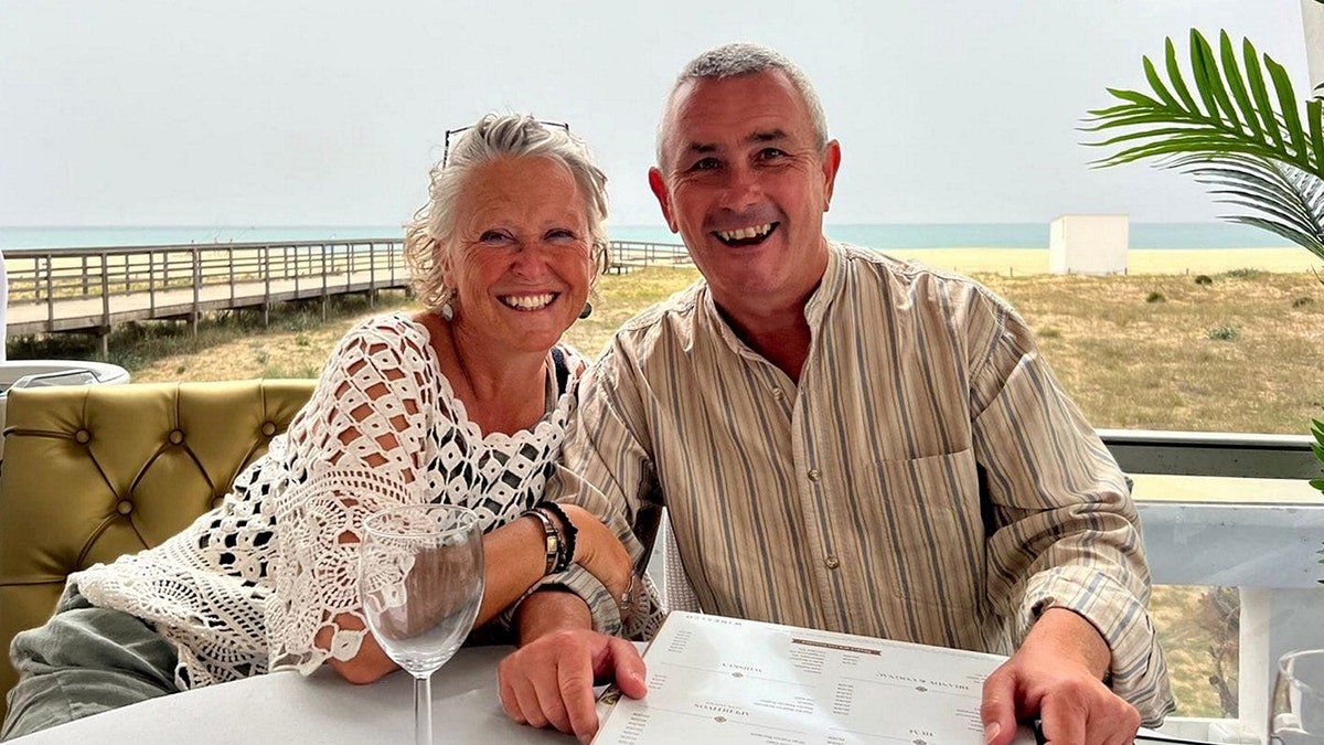 Karen and Myles Davies smiling and sitting at a restaurant on the beach.