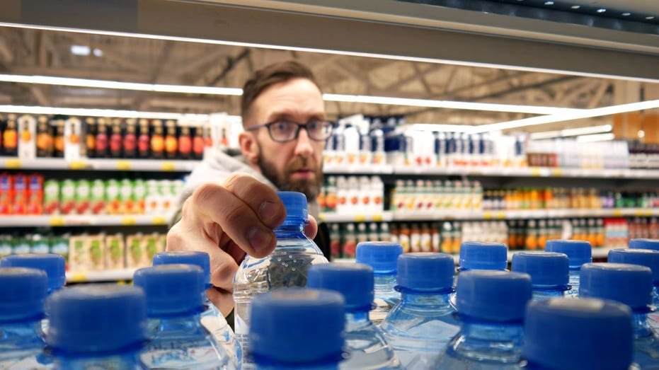 A man grabs a water bottle from a shelf.