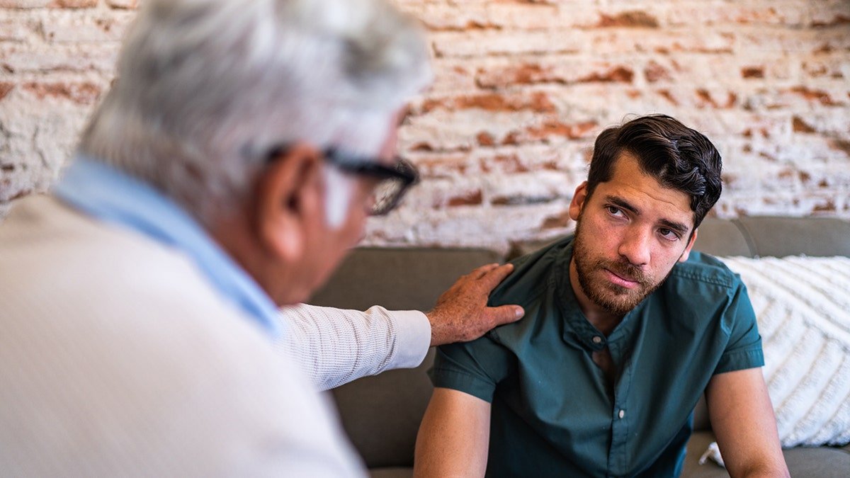 Young patient man talking to psychotherapist during therapy session at clinic