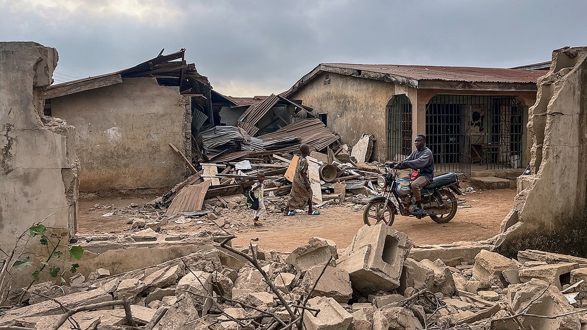 A motorcyclist and a person amid rubble of a destroyed home