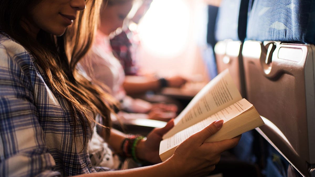 Unrecognizable woman smiling reading a book during her flight.
