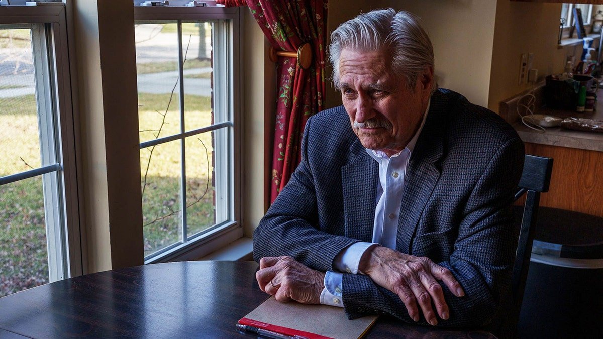 Larry Sells looking down in front of a window.