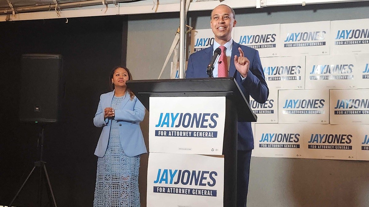 Jay Jones speaking at a podium with wife Mavis Jones standing behind him in Norfolk Virginia