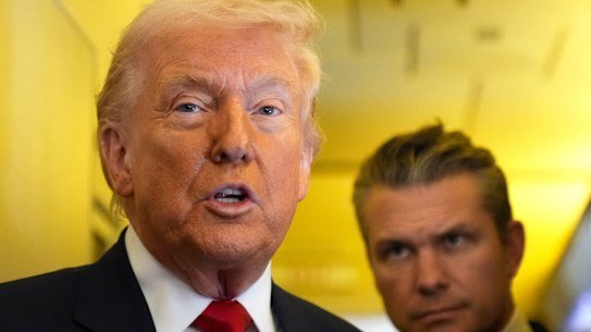 Donald Trump speaks to reporters as US Defence Secretary Pete Hegseth listens while travelling aboard Air Force One.