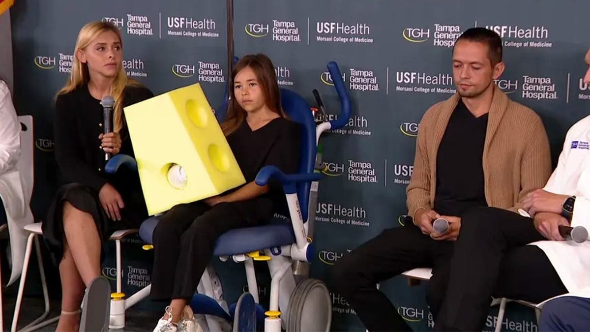 Leah sits with her parents during a hospital news conference.