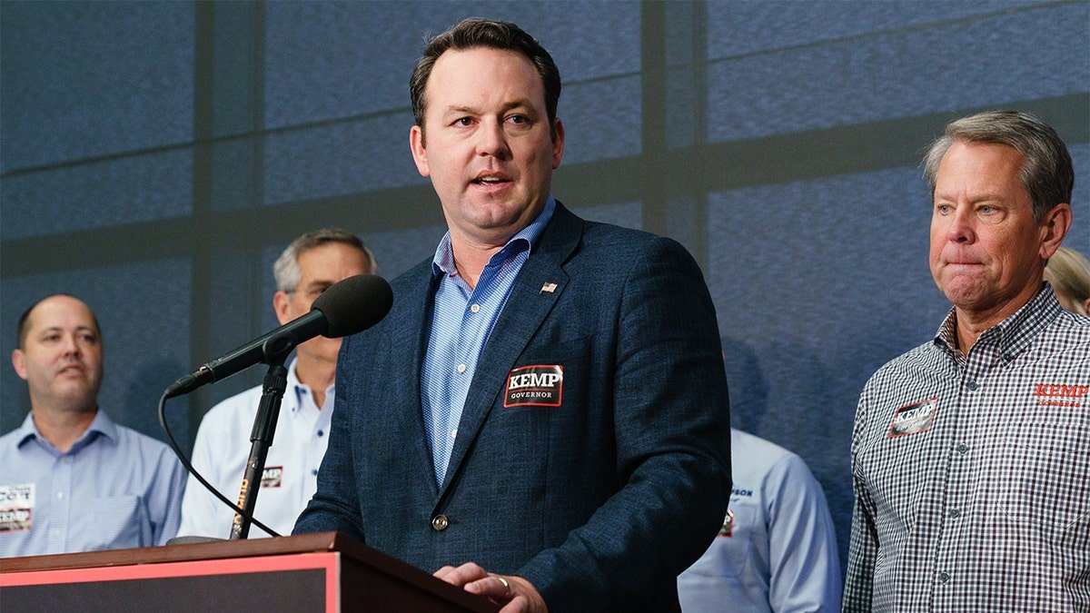 Burt Jones speaking at a press conference with Governor Brian Kemp listening in Atlanta
