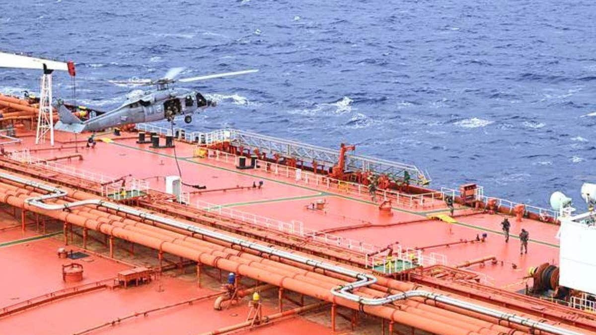 A white U.S. military helicopter hovers over the bright orange sanctioned stateless crude oil tanker M/T Tifani during an U.S. interdiction.