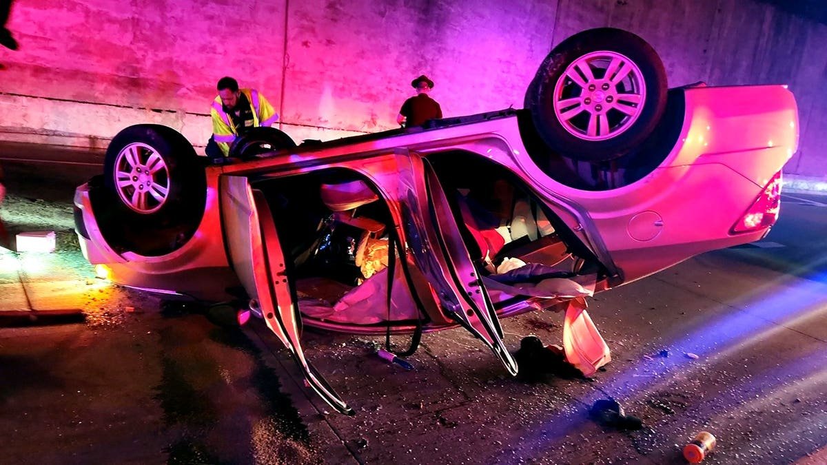 overturned car on interstate with doors open and surrounded by emergency responders