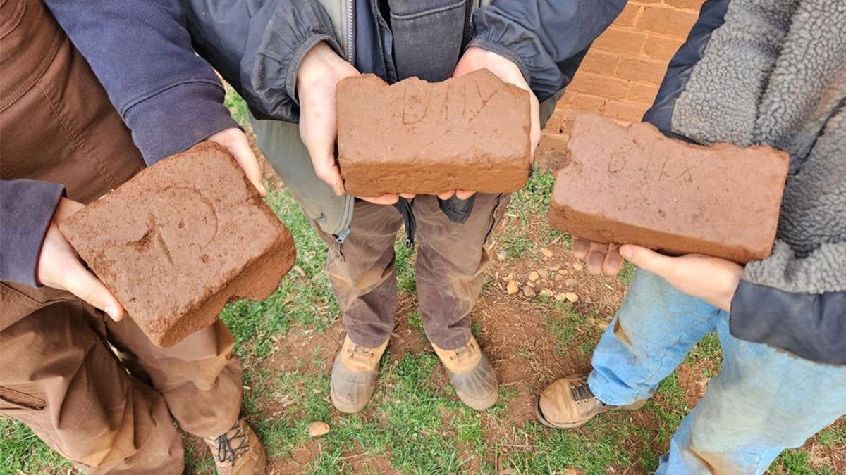 Three archaeologists holding three bricks outside kiln