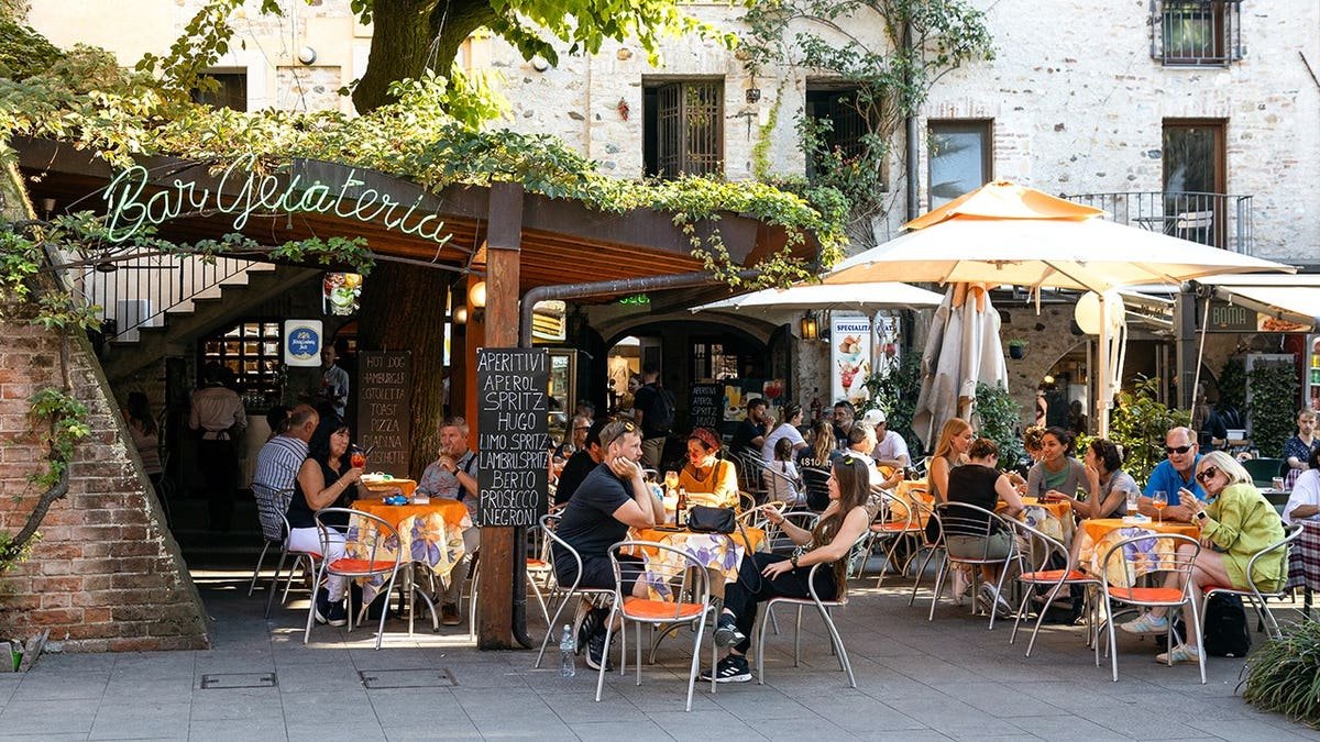 People enjoying aperitivo at an outdoor gelateria shaded by trees in Sirmione, Italy
