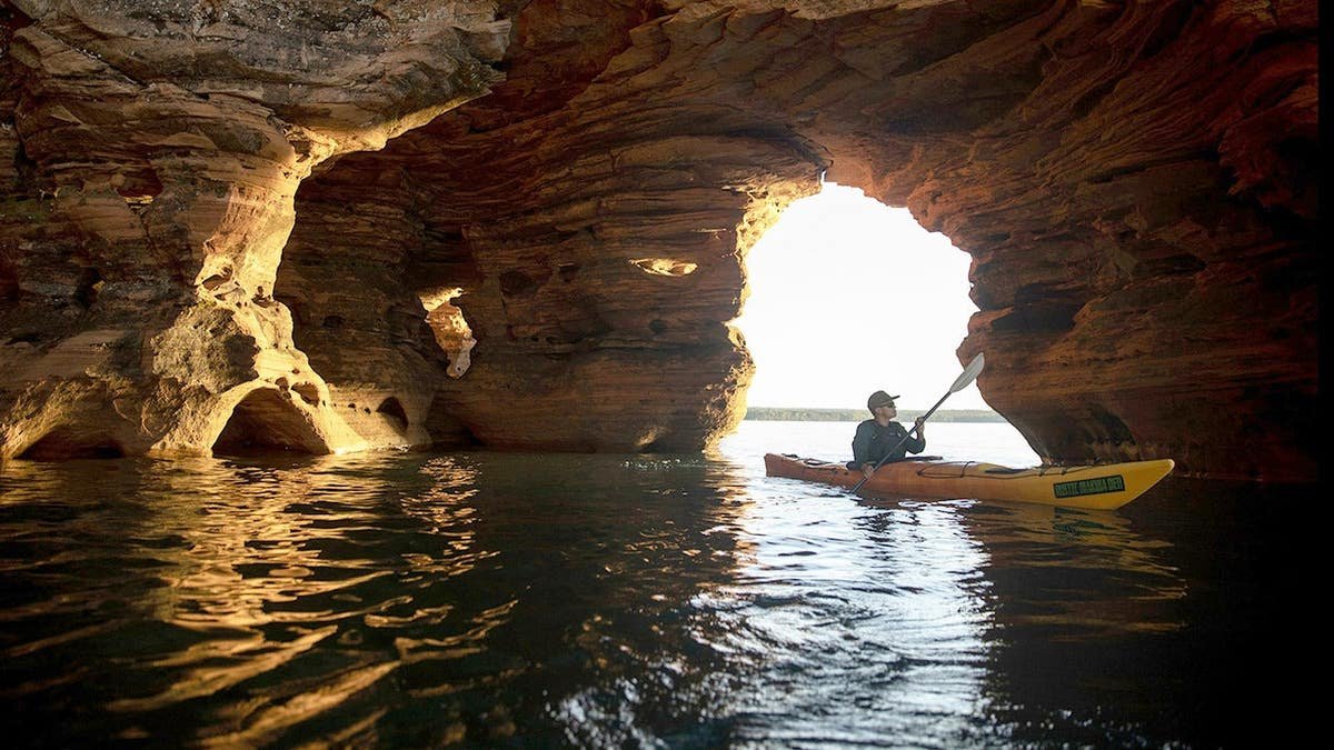 Man kayaking through Bayfield Peninsula Sea Caves in the Apostle Islands Maritime Cliffs State Natural Area in Wisconsin.