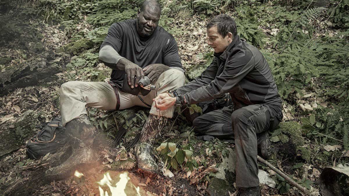 Bear Grylls and Shaquille O'Neal sitting at a bonfire during filming.
