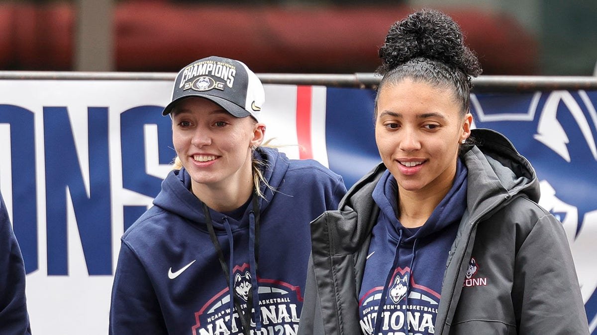 UConn student-athletes Paige Bueckers and Azzi Fudd walking onto stage outdoors.