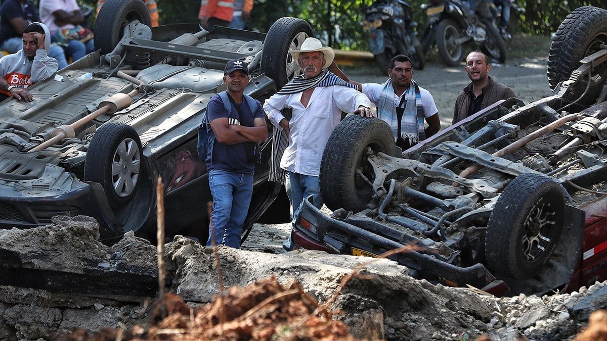 People look at vehicles damaged from an explosion.