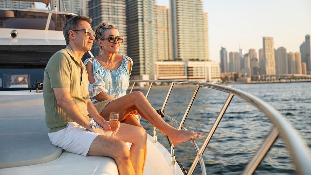 A cheerful couple in their 50s sits with wine on a private yacht, relaxing with wine.