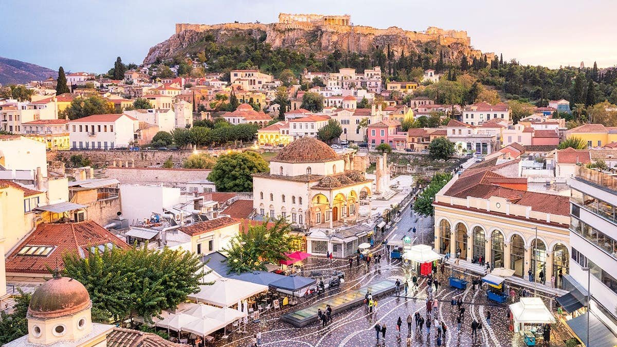 People walking in a square with the Ancient Greek Parthenon on the Acropolis in the background