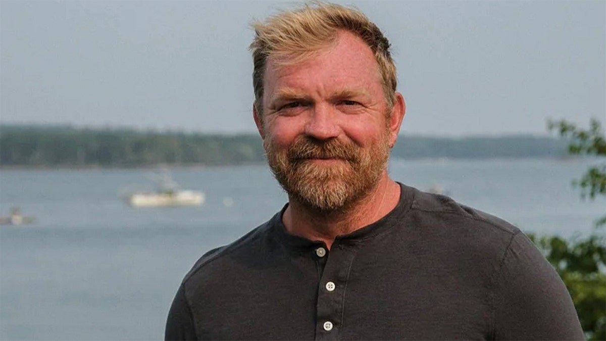 Graham Platner standing outdoors wearing a blue shirt