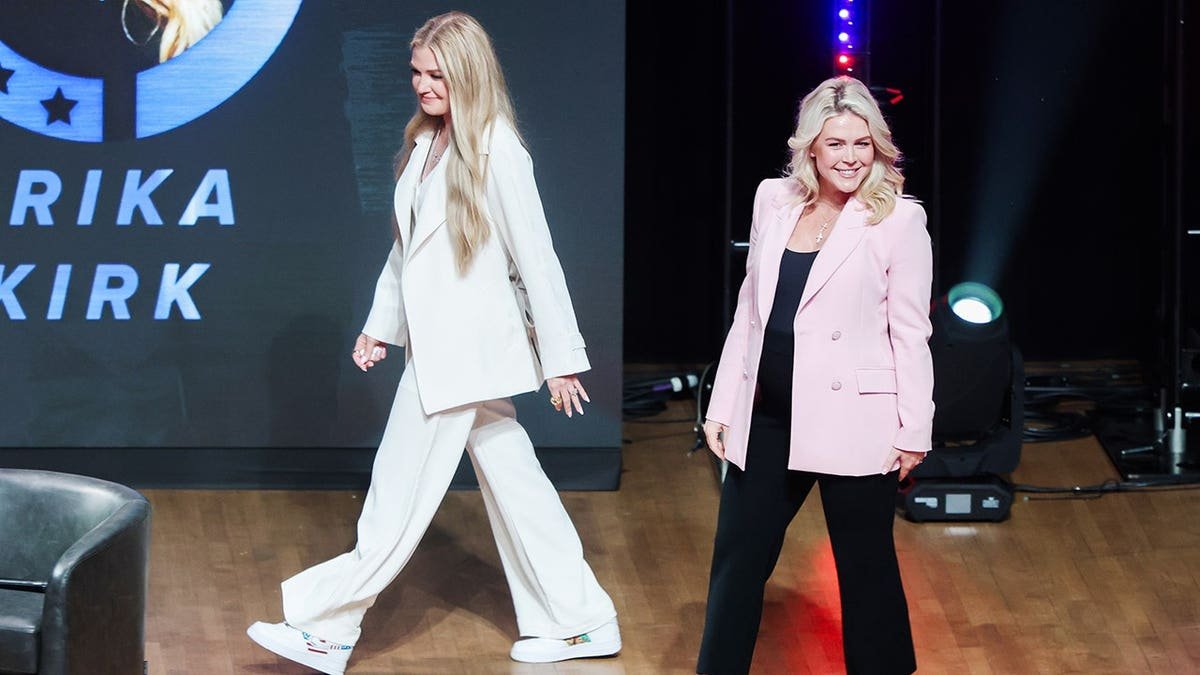 Erika Kirk and Karoline Leavitt walking onstage at George Washington University auditorium.