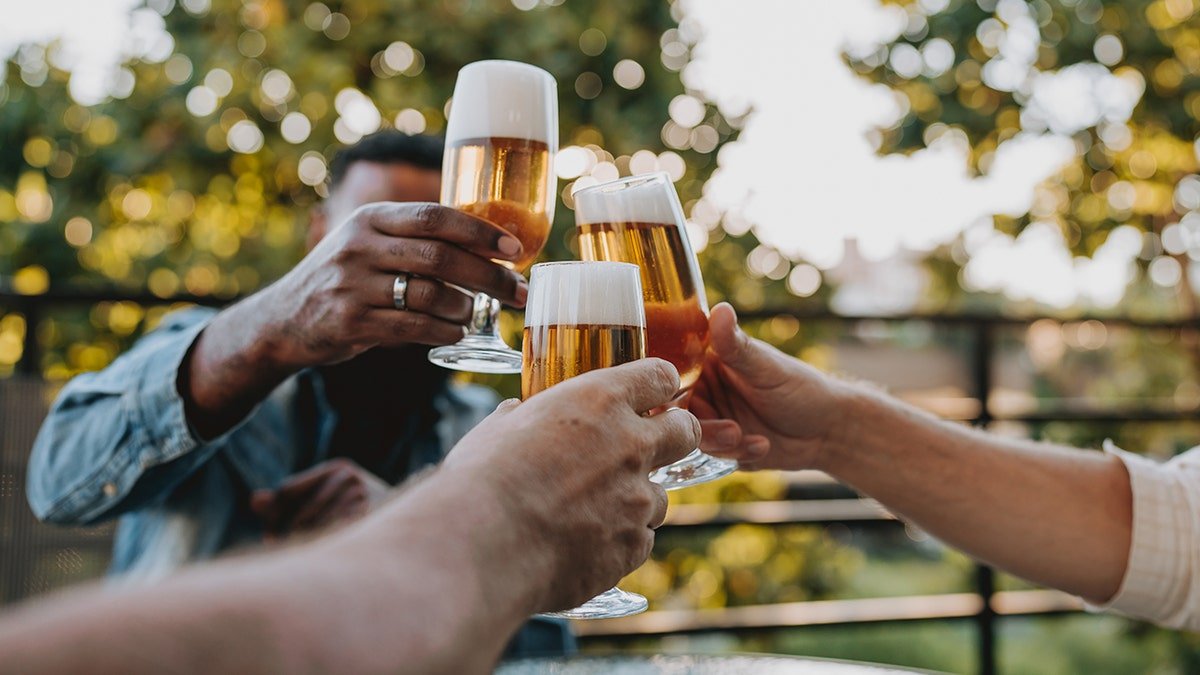 Three men clinking beer bottles together outdoors.