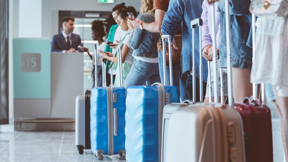 Travelers with luggage using smart phones while waiting in line at airport
